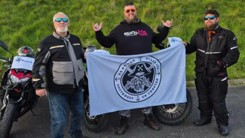 Joanne Smith Christopher Smith is pictured with his father and brother in law. All three men are wearing biker gear and they are holding a banner between them that says Bearded Villains South West UK Chapter. They are standing in front of their motorbikes.
Each motorbike has a small sign on the front that says Mind with a little blurb about their fundraiser.
