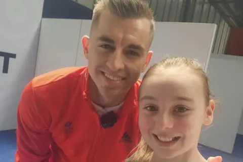 Family photo Amelia is posing with Max Whitford. He's wearing bright orange. They're both smiling.