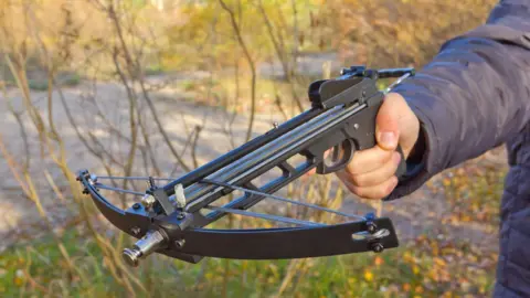 Getty A man points a crossbow towards the ground