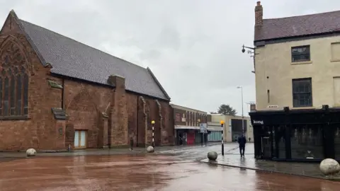 Coventry City Council A road junction, to the left is a church building with shops next to it, on the right is a building with a black frontage and a sign that says kong