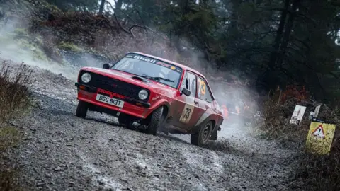 Bryan Laycock A red rally car skids on a mud track.