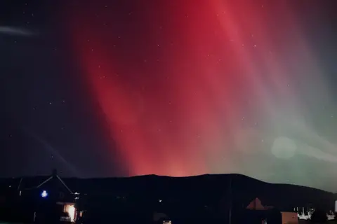 Josh / BBC Weather Watchers Sheets of red run diagonally through the sky, with a house and hillside in the foreground