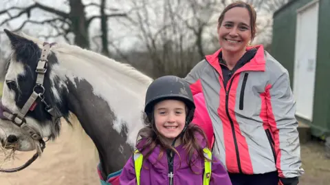 Evie and her mum Chantelle stand in front of their horse in high vis clothing. Dixie is looking to the left.