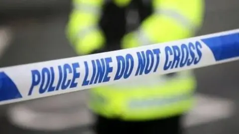 Generic image showing blue and white corden tape saying Police line - do not cross. Behind, blurred, is the outline of a police officer in hi-vis.