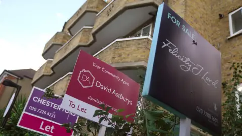 PA Media Two colourful 'to let' and one colourful 'for sale' boards outside a block of London flats