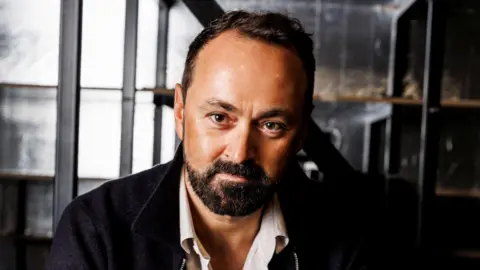 A head shot of Chris Stafford in a shirt and jacket