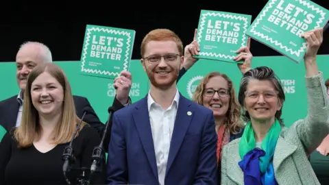 A group shot of smiling Green politicians holding up their election manifesto booklets 