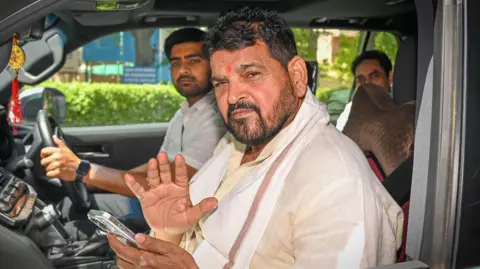 Brij Bhushan Sharan Singh seen in a car as he leaves a court in Delhi after appearing in an alleged sexual harassment case on 18 April 2024. He's sitting next to the driver, wearing a white kurta. 