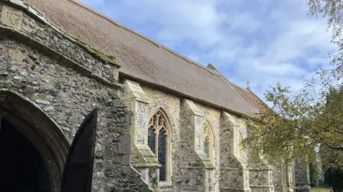 GUY CAMPBELL/BBC A side view of the church showing the opened door of the south porch, the stone buttresses and the newly-repaired thatched roof