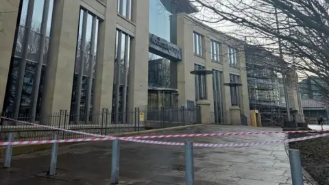 A large office building taped off with the sign Rockstar North above the door on a rainy day. 