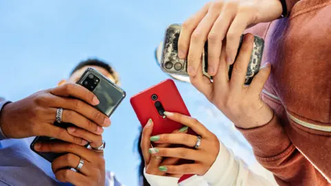 Low angle view of three young people using mobile phones outdoors.