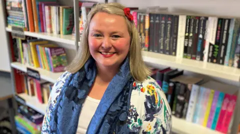 Prof Arlene Holmes-Henderson leads a department at Durham University dedicated to promoting the study of Latin and the Classics. She wears a blue scarf and a red flower in her blonde hair.