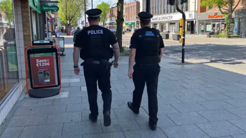 Matt Knight/BBC A picture of two male police officers with their backs to the camera walking along Brentwood high street.