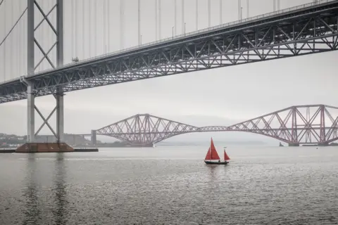 David Hatton Sailboat with a red sail below the Forth Road Bridge