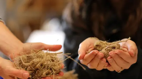 Yorkshire Wildlife Trust Close-up shot of two people's outstretched hands holding brown-coloured hessian seed bags 