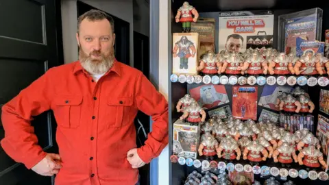 Amy Harrison Jamie Moakes posing like Ram Man with his arms flexed by his sides. His large collection of action figures is by his side.