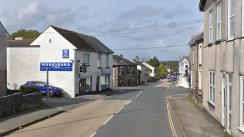 Fore Street in Bugle, with traffic lights, a shop on the left, and a cross-roads with a pub on the corner