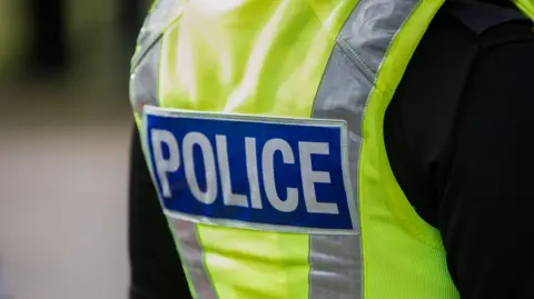 A zoom in of a police officer wearing a high-vis vest. It says "Police" on the back. 