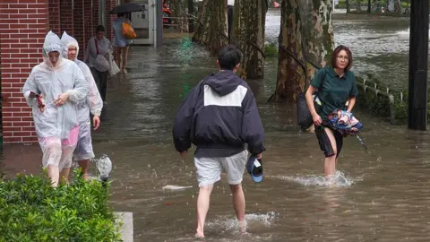 Getty Images Residents wade through flooded streets in Shanghai