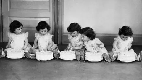 Getty Images Cinco crianças vestidas combinando sentam-se no chão em fila em frente aos seus próprios bolos