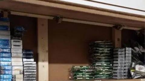 Kent Police Vapes and cigarettes pilled up in boxes behind a fake wall 