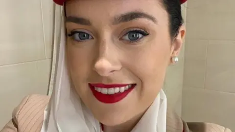 DETAINED IN DUBAI GROUP Tori Towey smiling at the camera. She has brown hair and eyebrows. Is wearing red lipstick and diamond stud earrings.