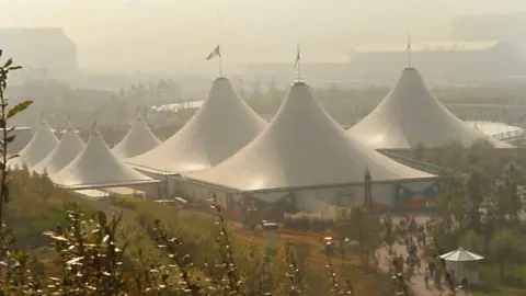 Potteries Museum and Art Gallery A series of large white tents - three very large and four smaller - are positioned among a lawned area which also includes flowerbeds. There is a train track running alongside the left hand side of the image. In the distance are some other buildings which are obscured by the hazy atmosphere.