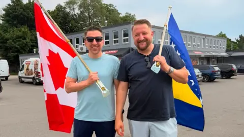 Supplied/Adis Mrakovic Amir and Adis Mrakovic smile, one holding a Canadian flag, one a Bosnian flag. They are in a parking lot and dressed casually in T-shirts.