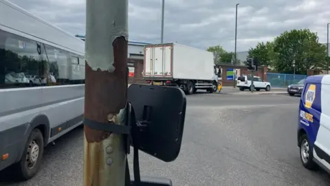 An image of the mirror strapped to a lamppost on the junction of Lady Bay Bridge and Meadows Lane. There are cars on either side of the island.