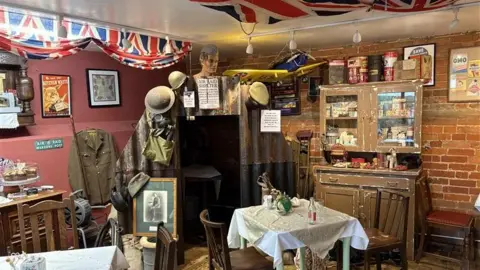 Jodie Halford/BBC A view of Nora's 1940s Tea Room. The walls have been decorated with 1940s items, clothing and banners.
