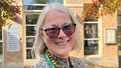 Picture of Christine Wise. She has white shoulder length hair and is wearing dark glasses