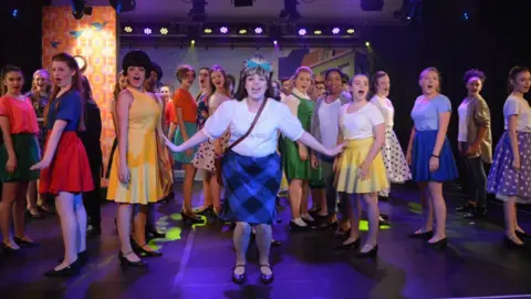 Viva! A large group of young people singing while wearing colourful outfits on stage.