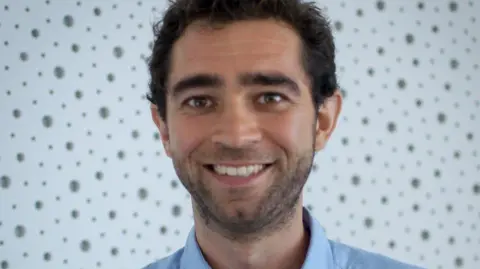 Miloš Fišar Dr Tommaso Reggiani wearing a blue shirt and smiling at camera