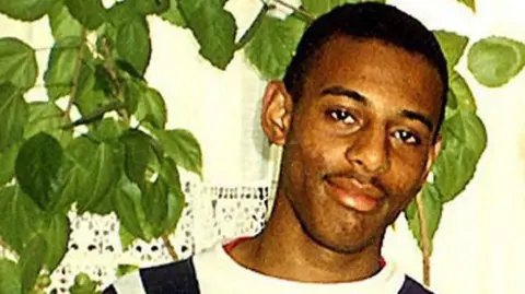 Family handout/PA An old, grainy photograph shows Stephen Lawrence standing in front of a large houseplant.