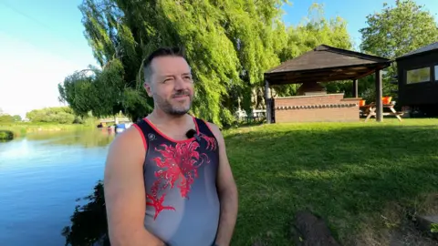 A man in a vest standing by a river.