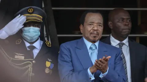 AFP applauds the 51st celebration of the Unity Day celebrations held in Yaounde on May 20, 2023 in the May 20 parade. He was wearing a blue suit and tie. A soldier pays tribute behind him.