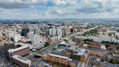 Getty Images An aerial overhead view of the city of Glasgow. The city’s motorway cuts through the urban core with busy traffic and surrounding modern and historic architecture. There are a mixture of high-rise offices, traditional sandstone buildings and civic landmarks with domed roofs. 