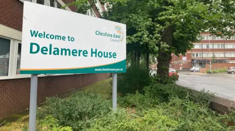 A view of Delamere House in Crewe. The image shows a brick building with a Cheshire East Council sign outside it.