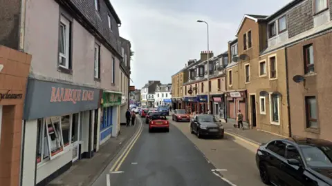 A street with shops on both sides and cars going down the road in both directions 