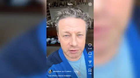 Instagram/Jamie Oliver Une capture d'écran de la vidéo Instagram de Jamie Oliver où il parle du fromage volé. Il montre Jamie Oliver, un homme aux cheveux gris courts, portant un cardigan à rayures bleues et un t-shirt bleu.