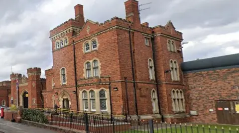 Google Victorian frontage of the red-bricked HMP Lincoln prison building with black railing in the foreground and high wall to the side