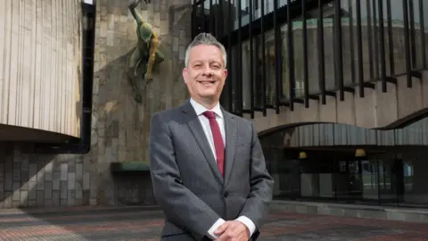 Newcastle City Council A man in a dark grey suit and a red tie