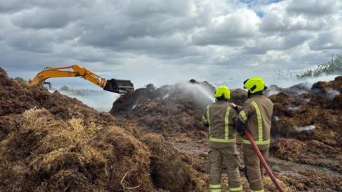 Two firefighters spray water on the haystack