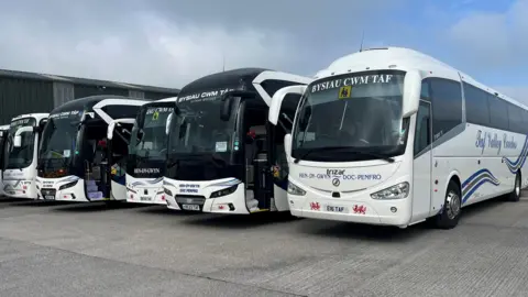 A row of buses from Taf Valley Coaches parked on concrete at the company depot