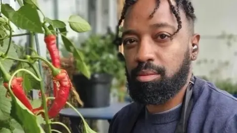 Jason Williams is sitting on his balcony surrounded by a variety of different plants.