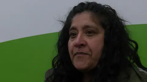 Dave Edwards/BBC A woman with black hair standing against a white and green background