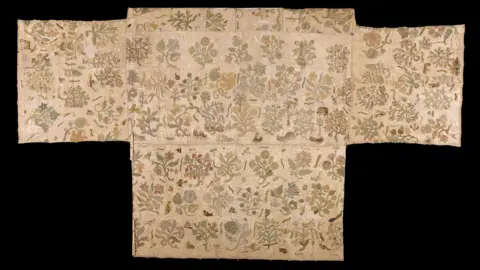 Historic Royal Palaces/Courtesy of St Faith's Church, Bacton A photograph of a piece of white embroidered cloth pictured against a black background. It has a floral design on it