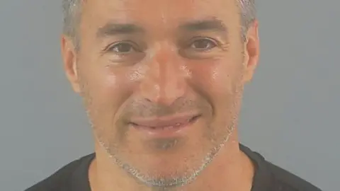 A police custody photo shows Peter Black smiling. He has brown eyes and grey hair and whiskers.