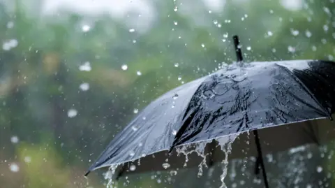 An umbrella being held in a downpour of rain. You cannot see who is holding it, just rain running off the black umbrella itself.