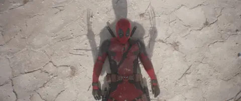 Disney Deadpool jogado no chão enquanto a sombra das garras do Wolverine se eleva sobre ele